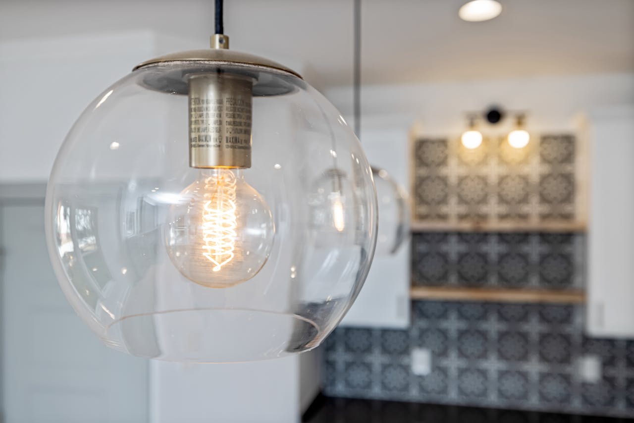 why-choose-us Close-up of a glass pendant light bulb illuminating a stylish, modern kitchen interior.