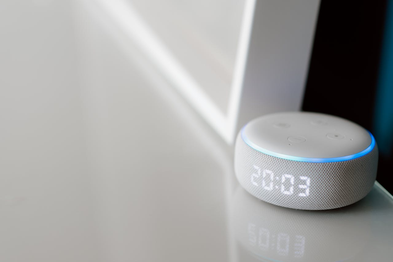 Close-up of a smart speaker with a digital clock display on a minimalist surface.
